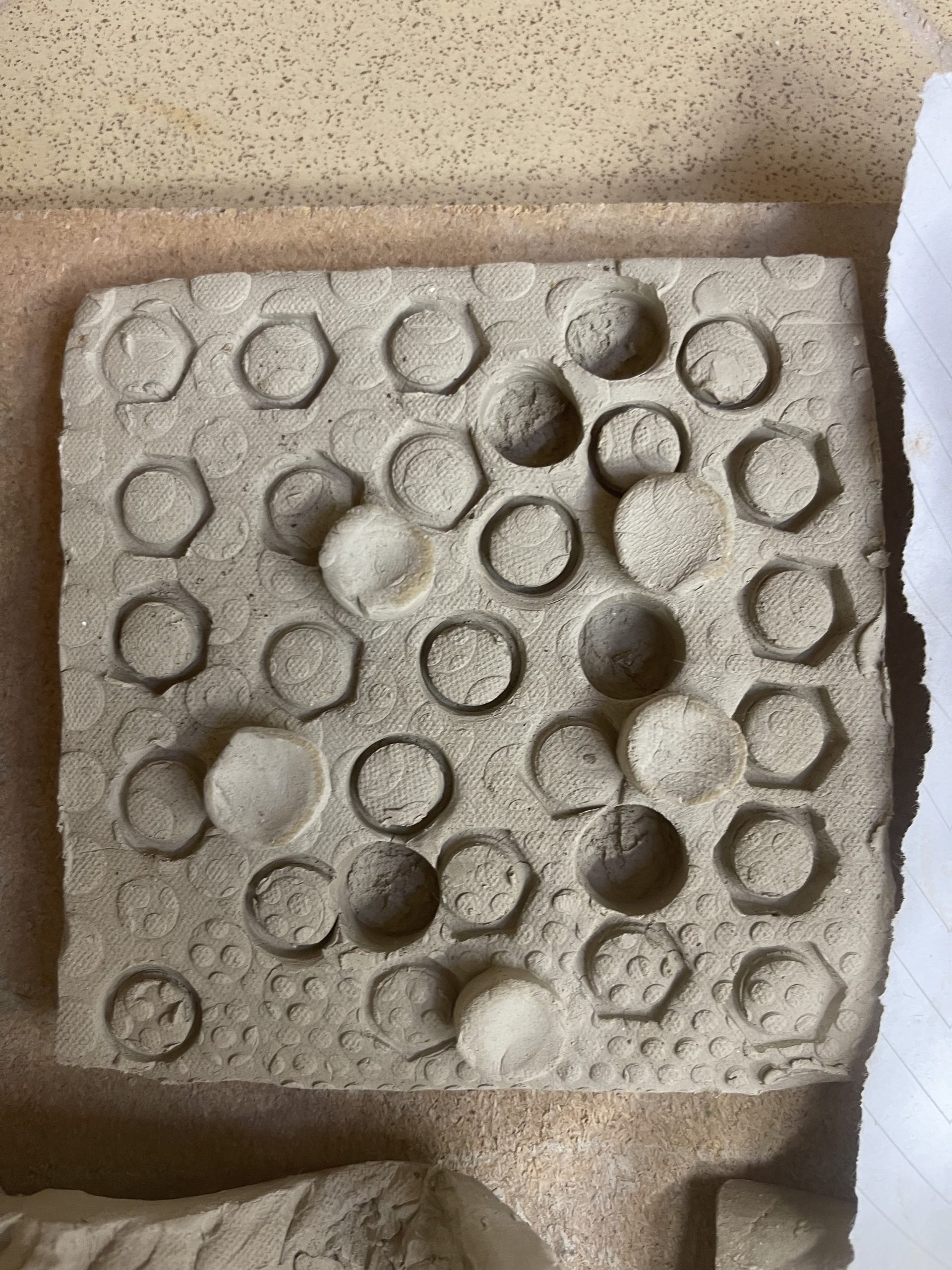  Using a metal bolt I pressed it into leather hard clay to bore segments out of the clay creating an inverted texture . Using another metal object with smaller indentations played on top of the original indentations made the texture appear busier almost like a busy factory . 
