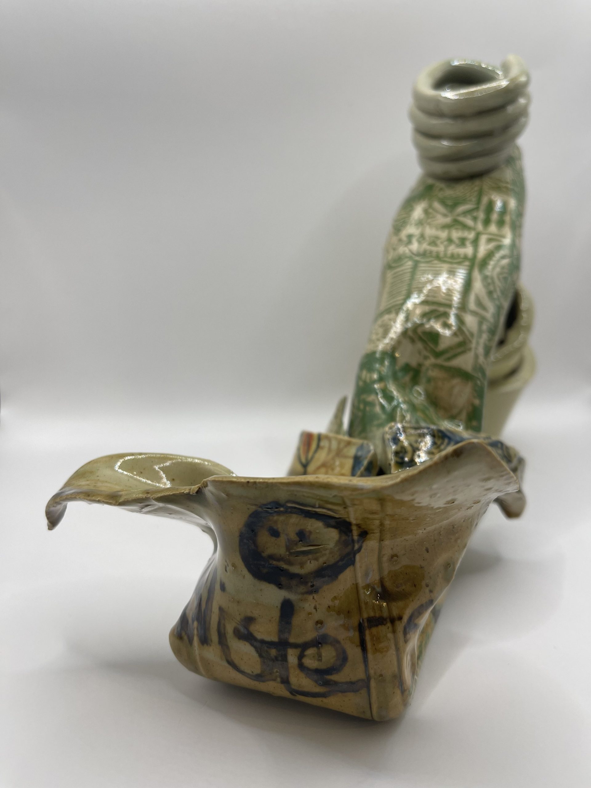  Manipulated extruded shapes decorated with underglaze decals and free hand lettering . A busy piece of work that conveys discomfort . 