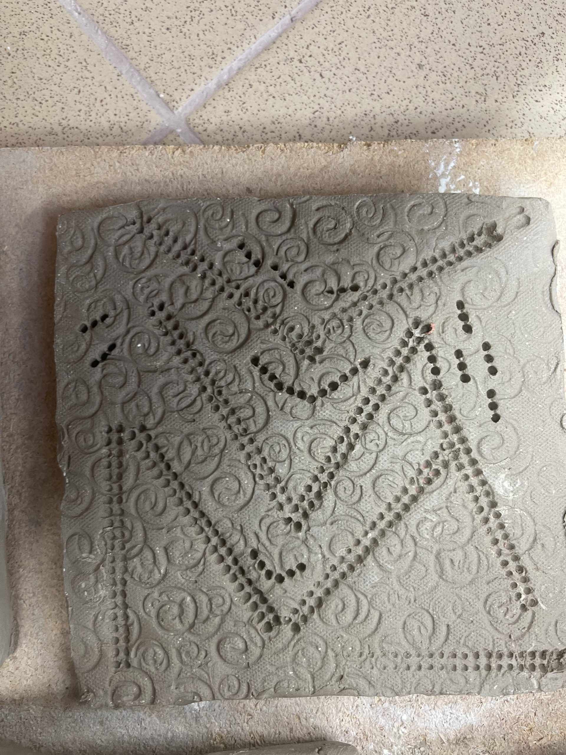  A leather hard tile was stamped into using lego bricks to create straight lines into the shell impressions. This made the tile texture to be linear but with a soft curly back ground. 